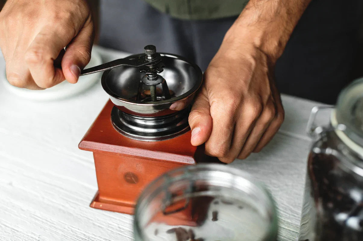 artisan kahve çekirdeklerini öğütmekte olan bir barista elleriyle el değirmenini kullanıyor.